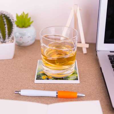 A glass with Whisky on top of a ceramic coaster on a work desk