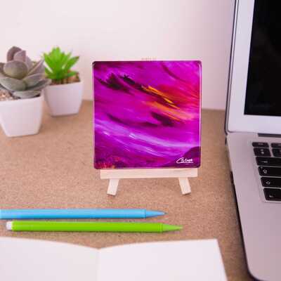 Mini easel holding a ceramic coaster of Moorland vale - a purple sky and moorland with an orange sun peering though