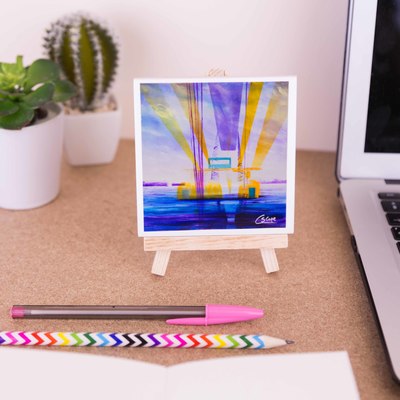On a mini easel is a ceramic coaster of the painting Transporter Bridge, Sunshine