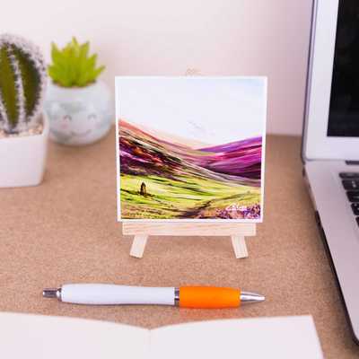 On a mini easel is a ceramic coaster of the painting Trekking