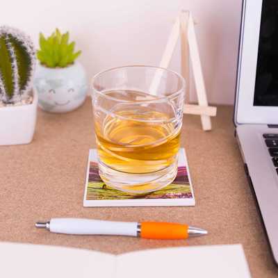 On a desk is a whisky tumbler on top of a ceramic coaster of Trekking