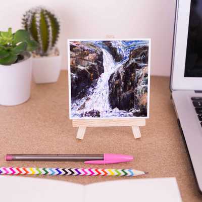 On a mini easel is a ceramic coaster of the painting Waterfall